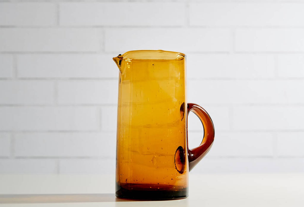 Amber glass pitcher on a white tiled wall background