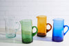 Four colorful glass pitchers on a white surface with a light-colored tile background