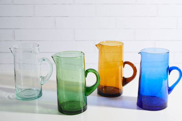 Four colorful glass pitchers on a white surface with a light-colored tile background