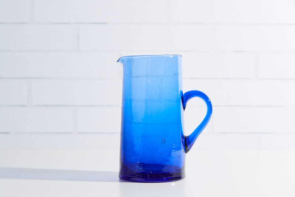 Blue glass pitcher on a white tiled background