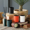 Decorative items including candles, a diffuser, and a plant on a wooden surface with a gray wall background.