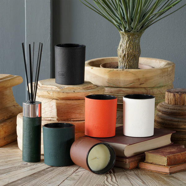 Decorative items including candles, a diffuser, and a plant on a wooden surface with a gray wall background.