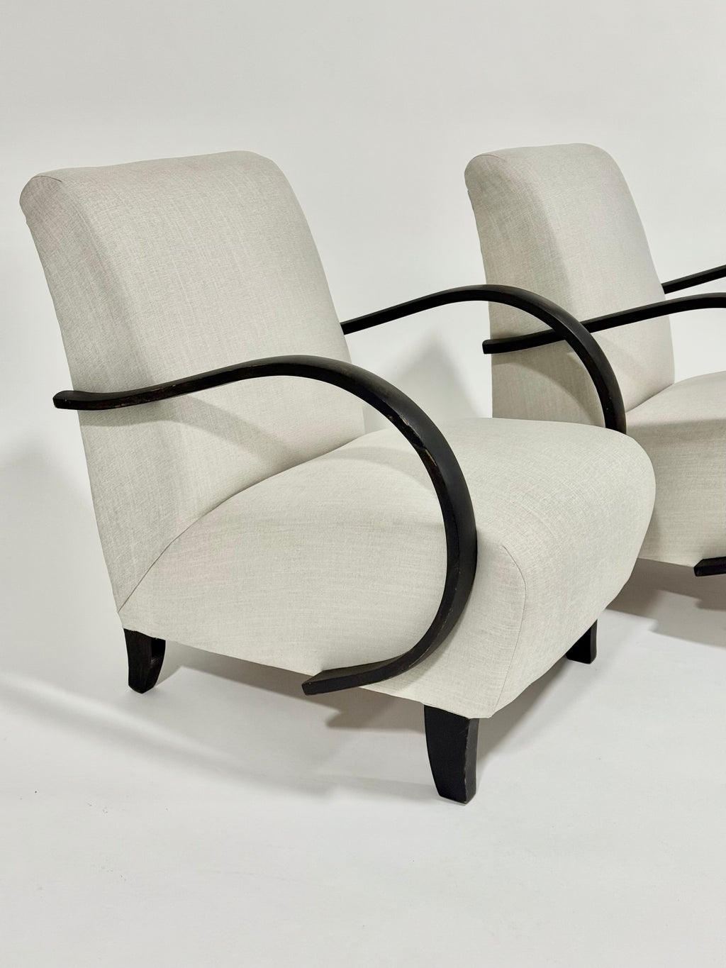 Two beige armchairs with black armrests on a white background