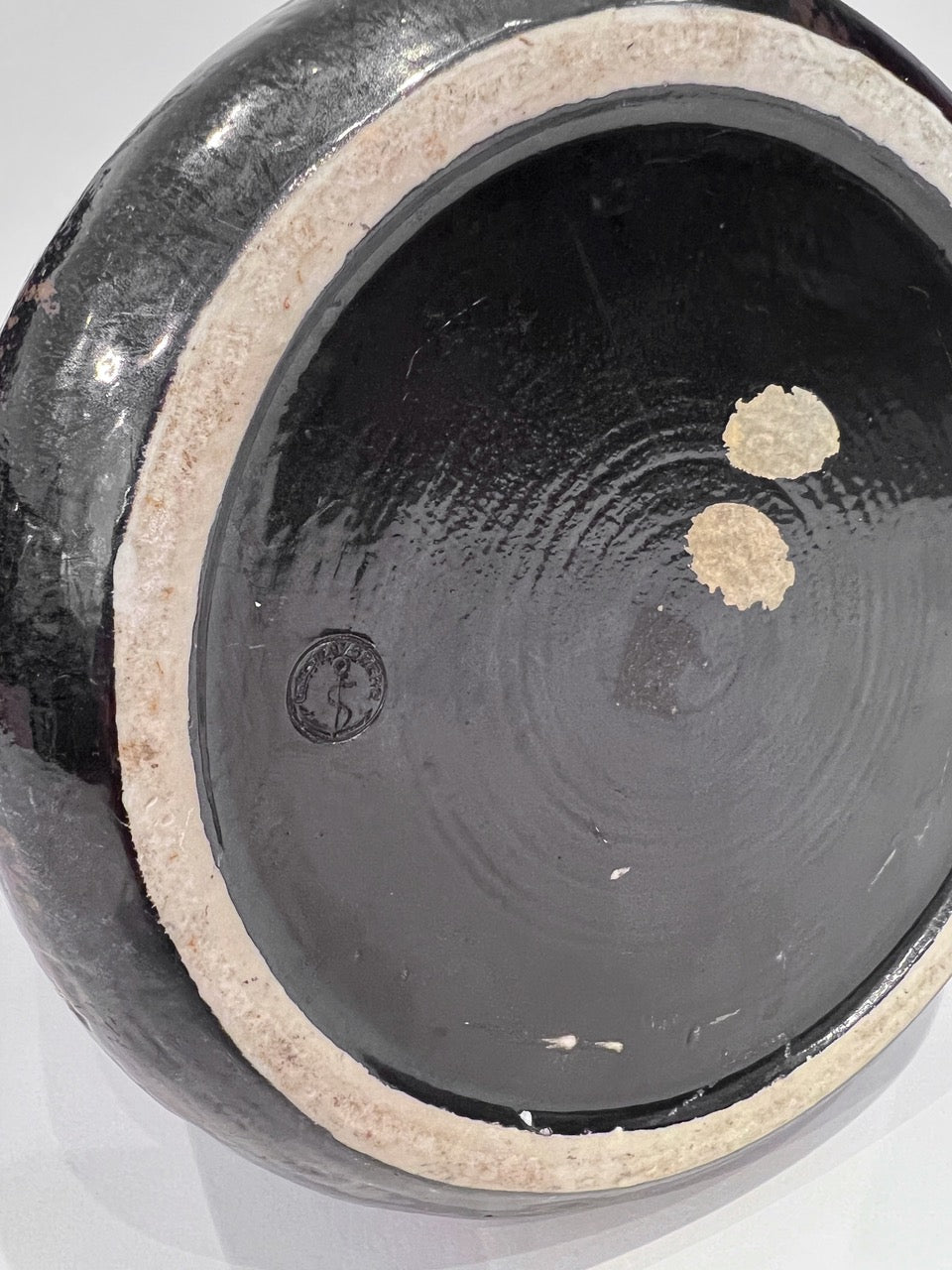 Close-up of a black ceramic vase with a beige interior rim on a white background