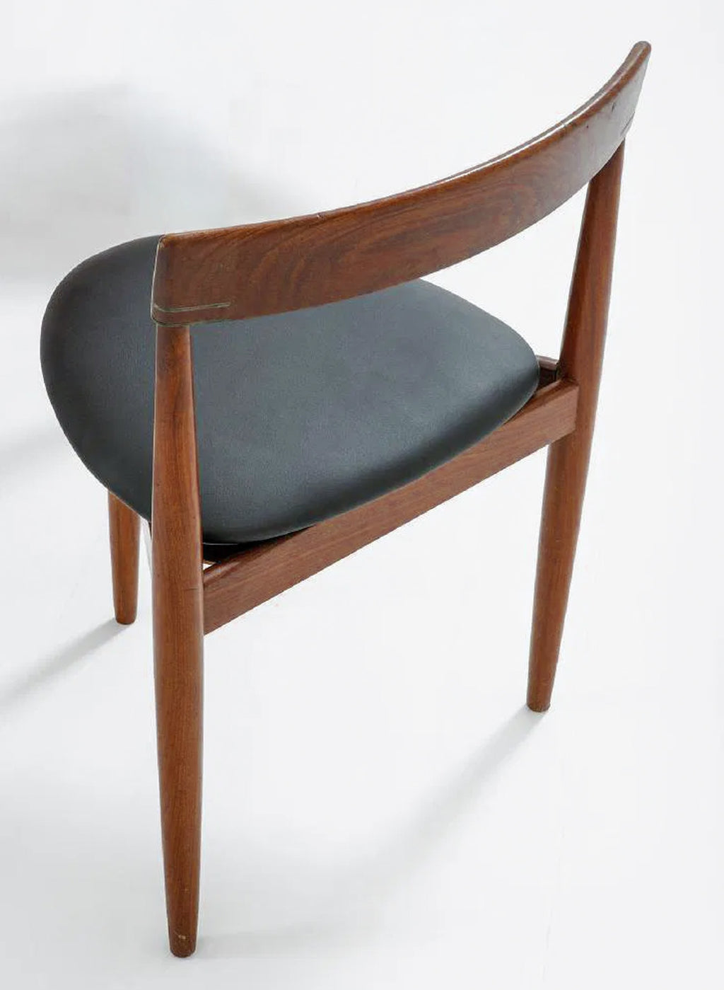 A mid-century modern wooden dining chair with a curved backrest, medium brown wood frame, and a dark gray upholstered seat cushion, shown from a three-quarters angle on a white studio background.