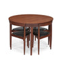 A round wooden dining table with four matching nesting chairs featuring dark cushioned seats, shown on a plain white background.