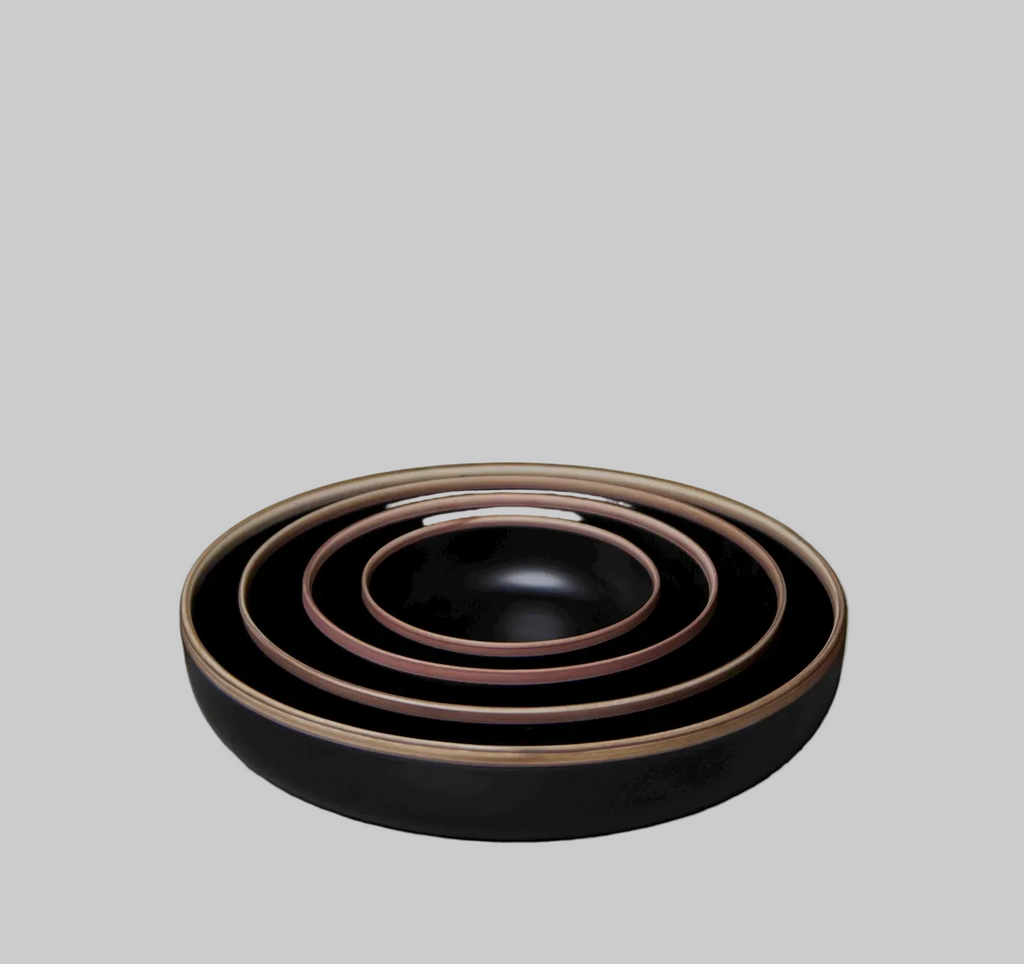 Set of three black ceramic bowls with bronze rims on a gray surface against a dark green background