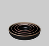 Set of three black ceramic bowls with bronze rims on a gray surface against a dark green background