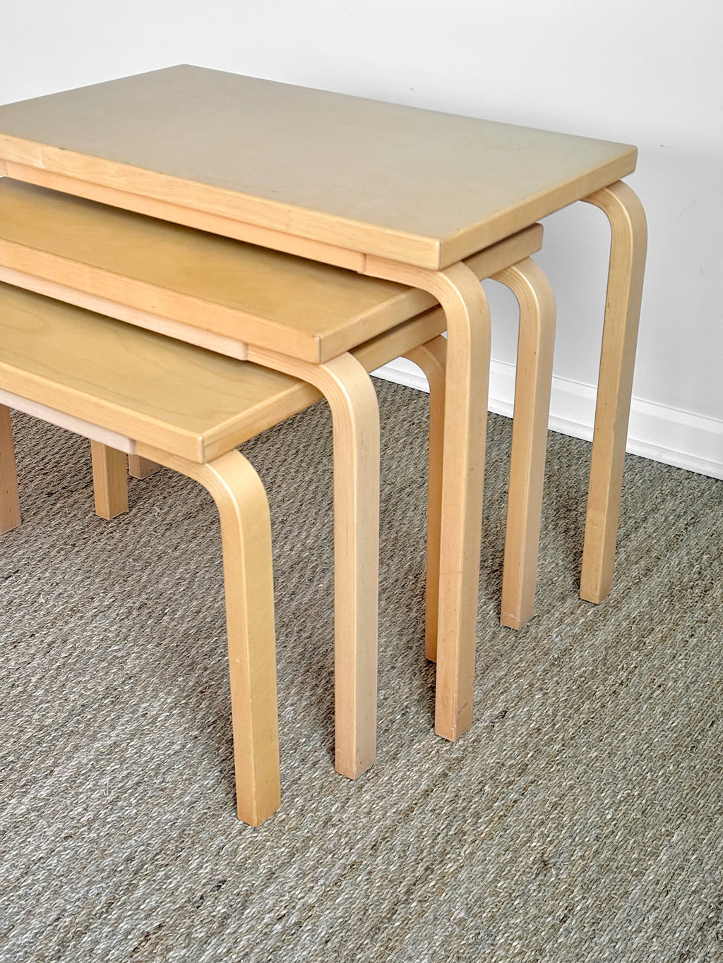 Set of three wooden nesting tables on a carpeted floor.