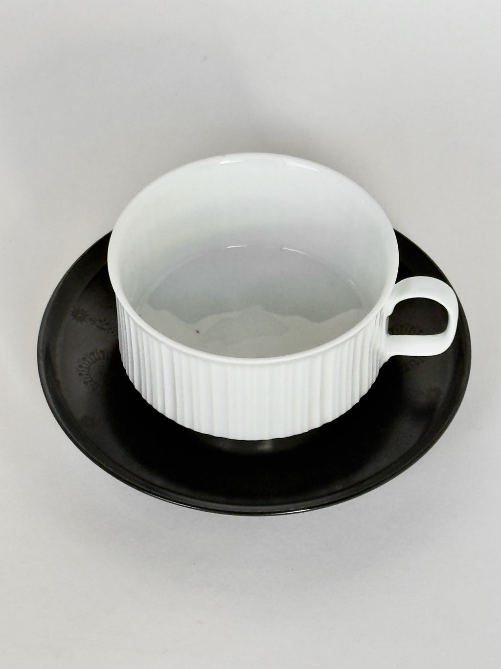 White ceramic cup with black saucer on a light gray background