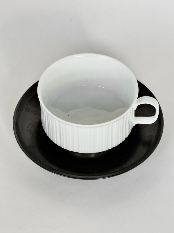 White ceramic cup with black saucer on a light gray background