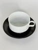 White ceramic cup with black saucer on a light gray background