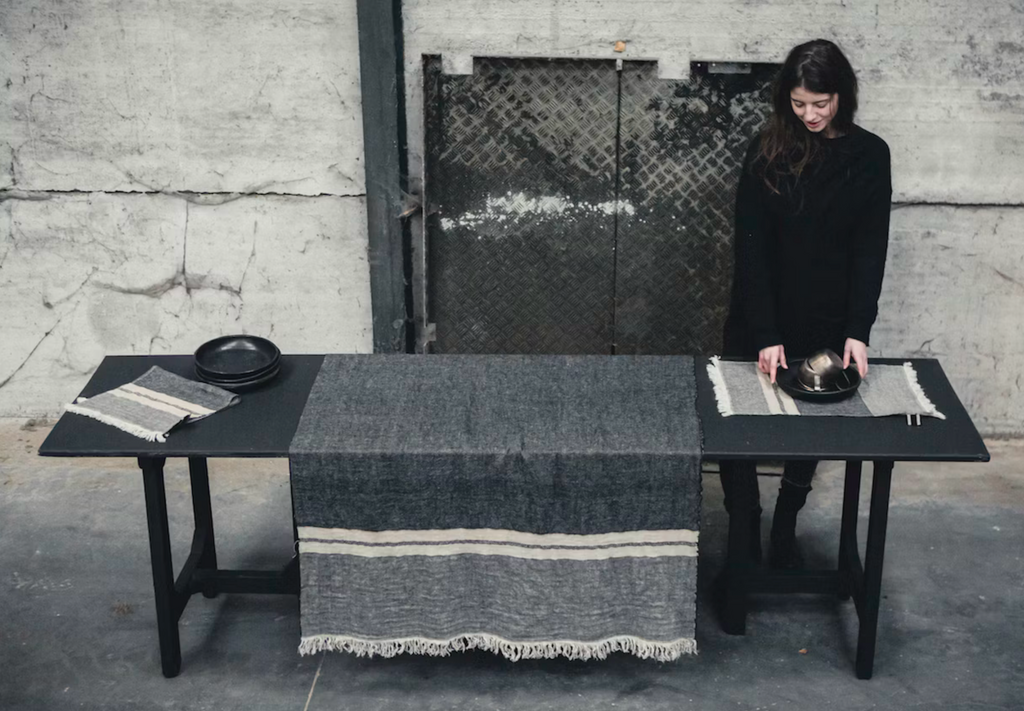 Person arranging items on a table with a textured tablecloth in a minimalistic setting.