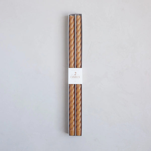 Two tall taper candles in packaging with a label on a light gray background
