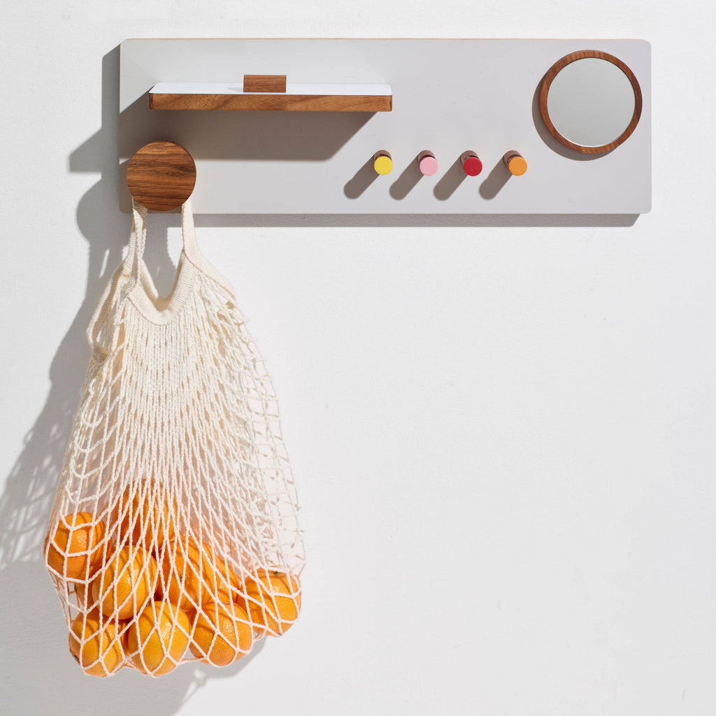 White wall-mounted shelf with wooden accents holding a net bag filled with oranges on a white background