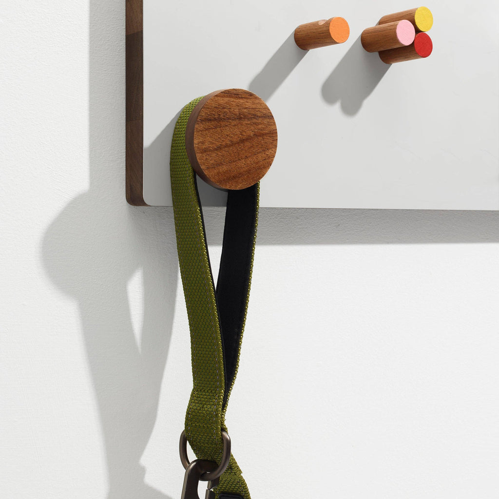 Wooden wall hooks with colorful ends on a white wall, one holding a green strap.