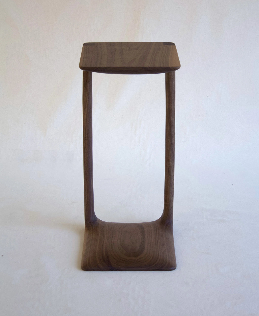 Wooden stool with a square seat and curved legs on a white background