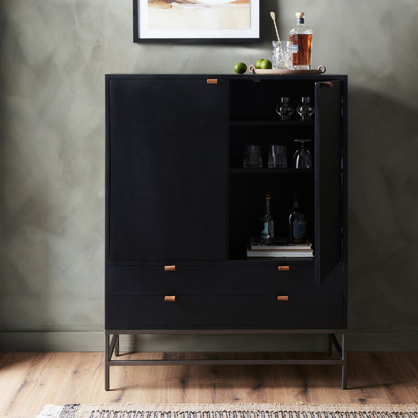 Black bar cabinet with open doors displaying bottles and glasses against a gray wall.