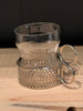 Clear glass mug with decorative metal base on a wooden surface