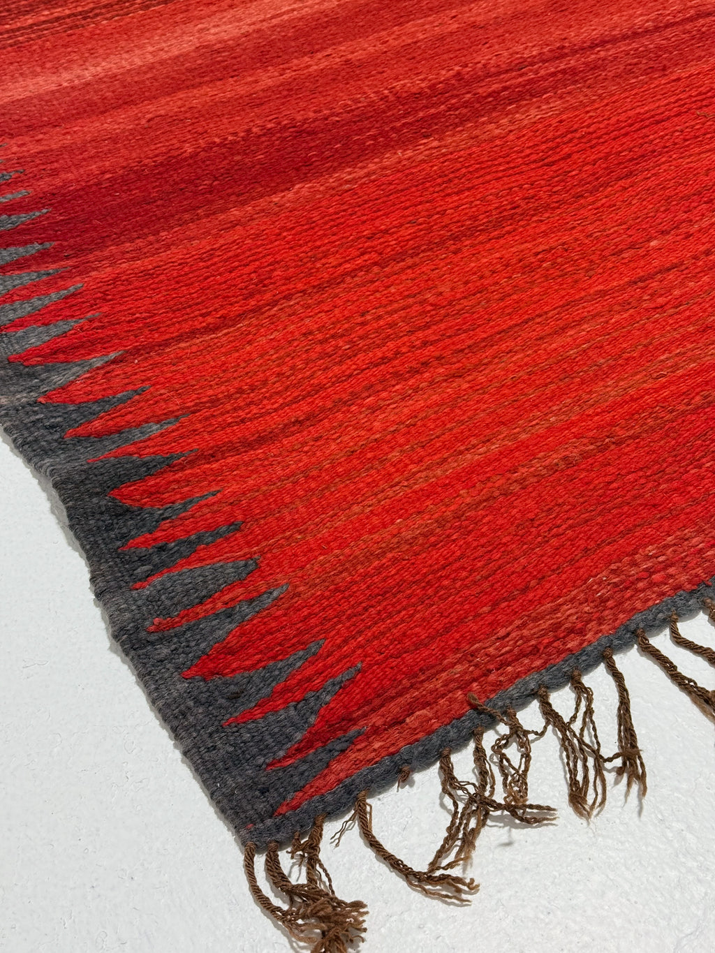 Close-up of a red and gray textured rug with fringes on a white background