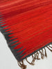 Close-up of a red and gray textured rug with fringes on a white background