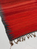 Close-up of a red and gray woven rug with fringes on a light background