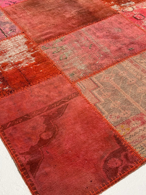 Patchwork rug with red and brown hues on a white background
