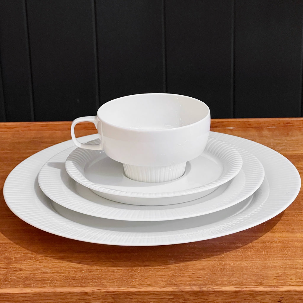 White ceramic dinnerware set on a wooden table with a black paneled background