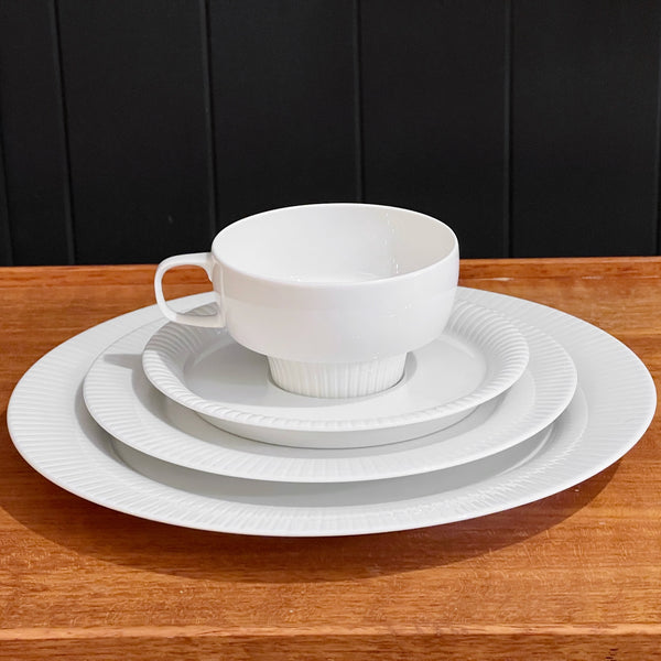 White ceramic dinnerware set on a wooden table with a black paneled background