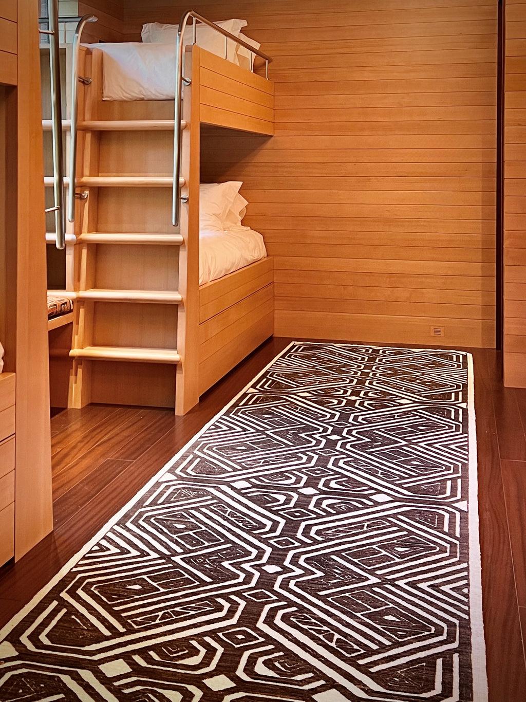 Wooden bunk bed in a room with a patterned black and white rug on the floor.