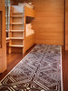 Wooden bunk bed in a room with a patterned black and white rug on the floor.