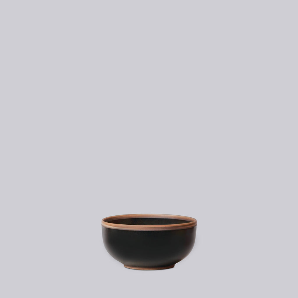 Black ceramic bowl with brown rim on a light gray background