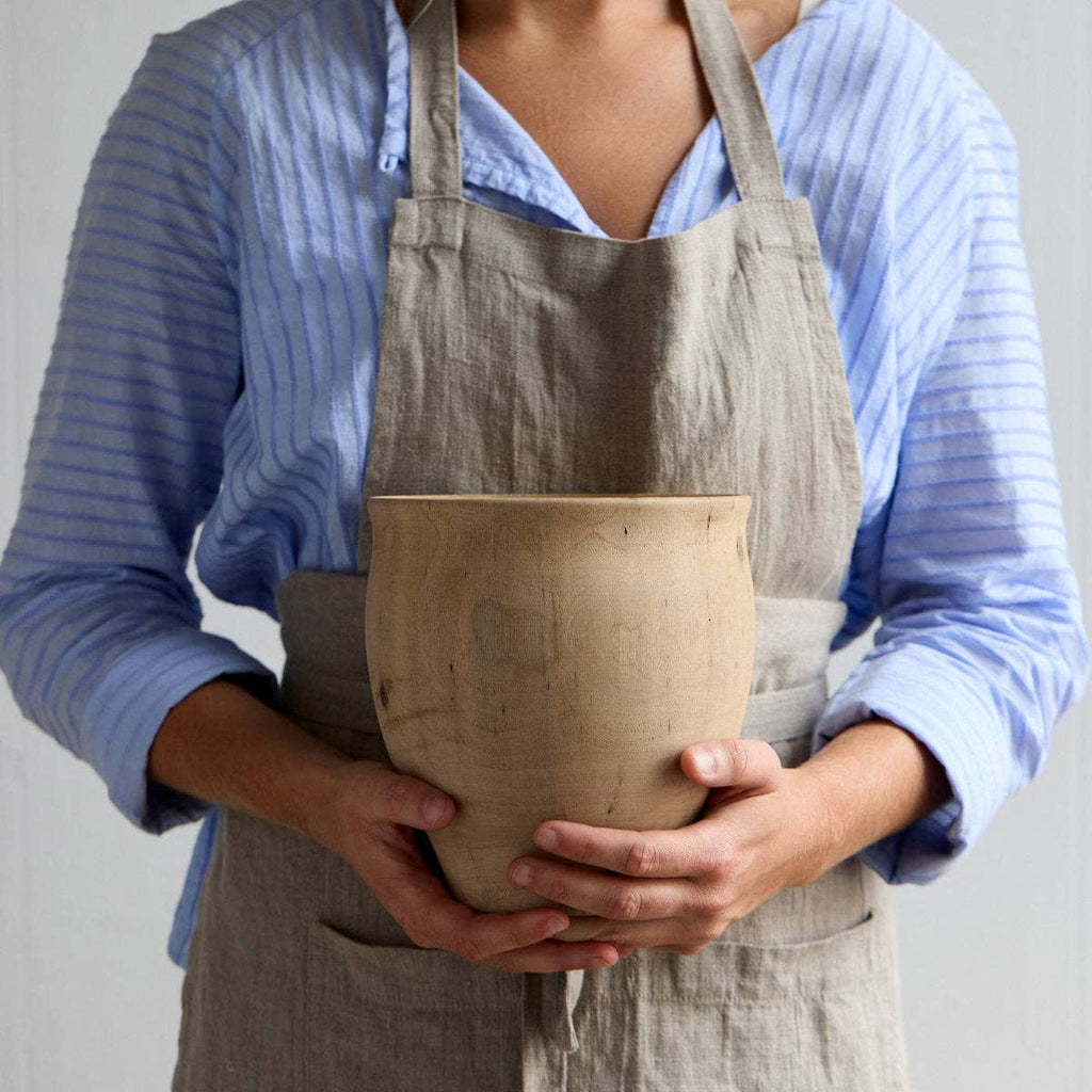 Person wearing a beige apron holding a ceramic pot against a neutral background