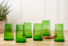 Set of green glass tumblers on a wooden surface with a white cabinet in the background.