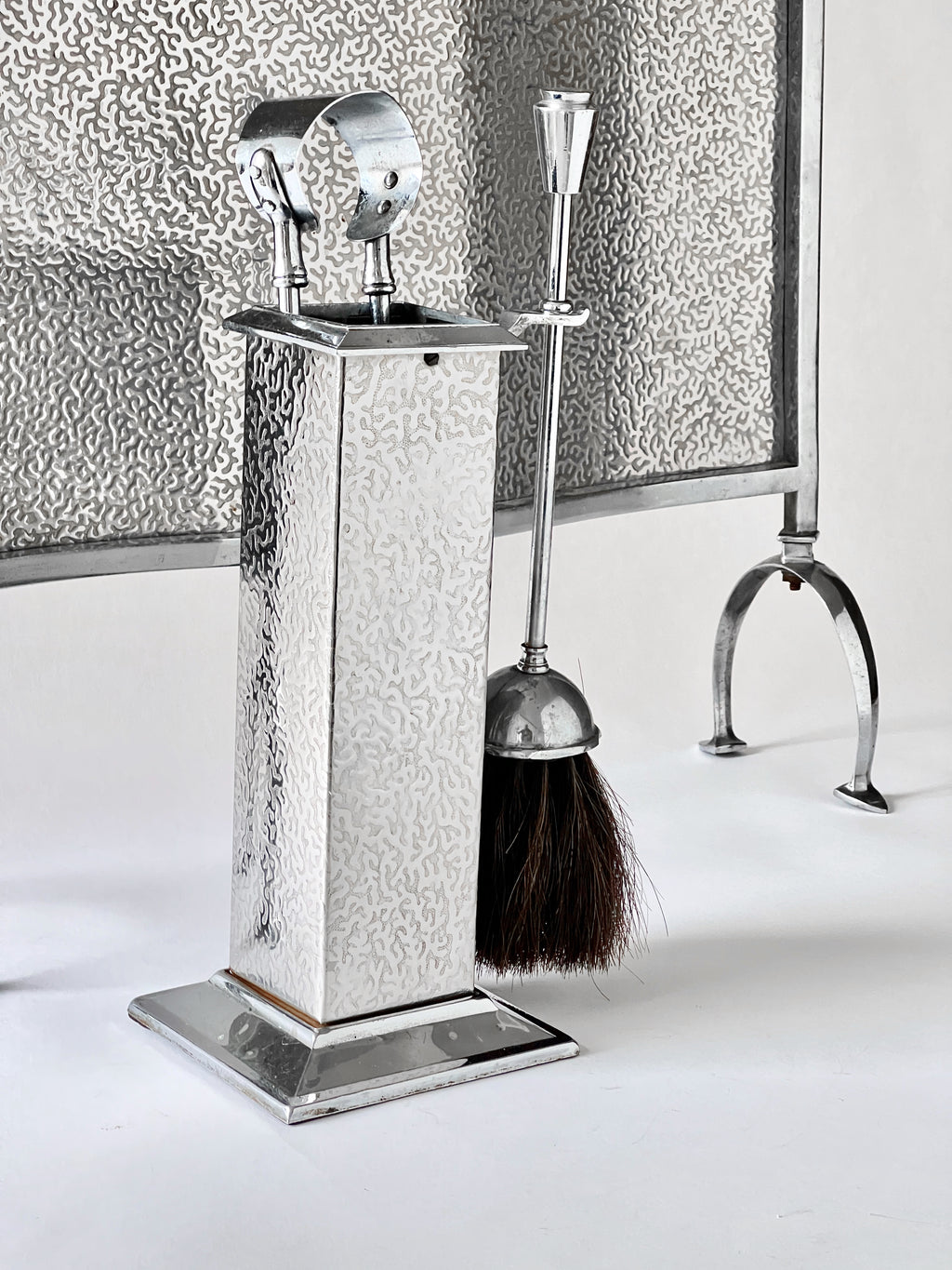 Decorative chrome fireplace tool set with broom and brush on a white background