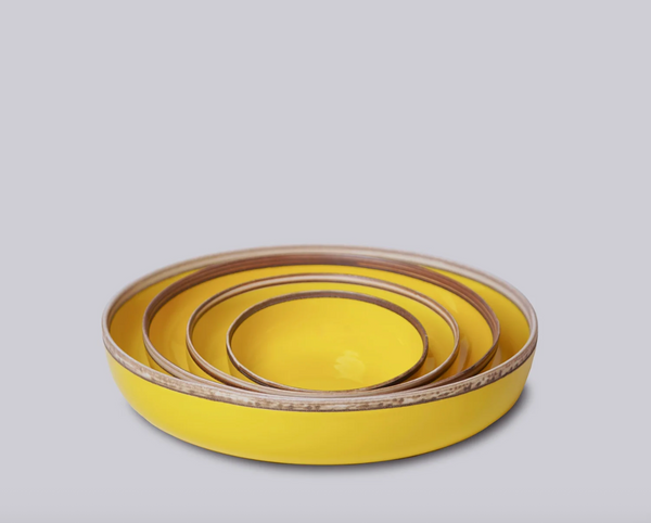 Set of three yellow ceramic bowls with brown rims on a light gray background
